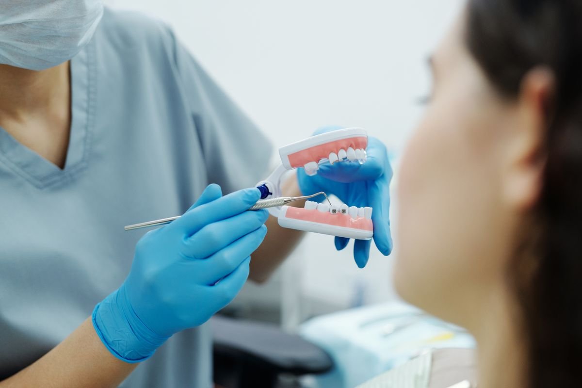 Dentista con guantes mostrando un modelo de dentadura a una paciente para explicarle el tratamiento de implantes.