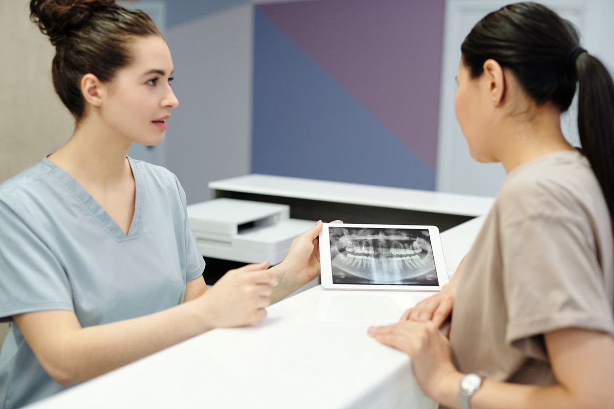 Dentista mostrando a la paciente una radiografía dental digital en una tablet para explicar el diagnóstico de una restauración.